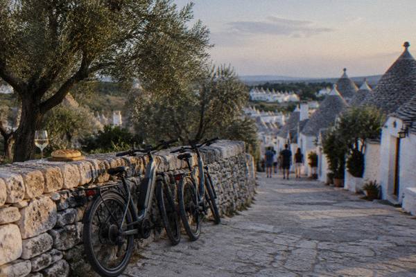 Two bicycles leaning on a dry-stone wall in olive groves near Alberobello, with wine and flatbread on the wall