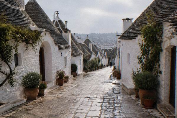 An early-morning cobbled lane lined with whitewashed trulli houses and potted plants in Alberobello