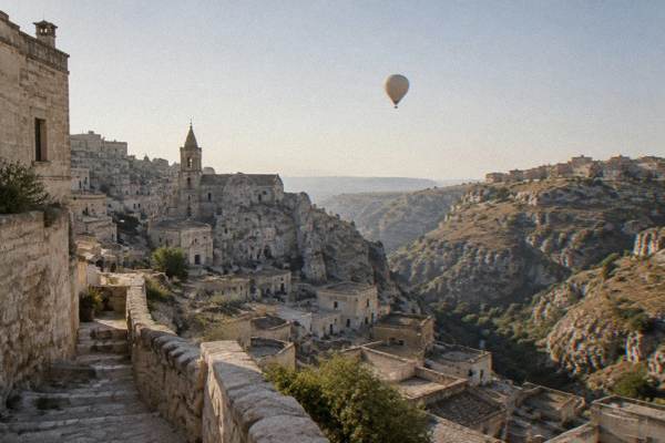 A hot air balloon rising in the dawn sky above the ravine and old town of Matera