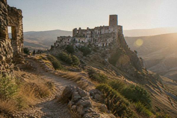 The abandoned hilltop village of Craco, crumbling stone houses and a square tower on a bare ridge, a few visitors on a path