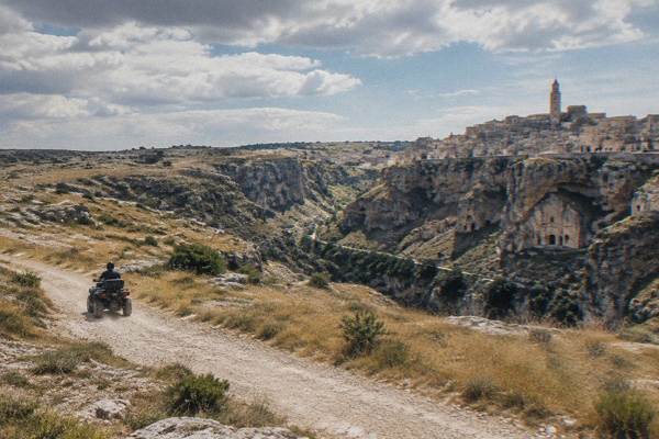 A quad bike on a dusty track across the dry limestone plateau near Matera, the rider seen from behind