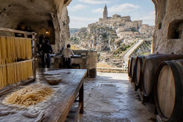 A rock-cut cellar with oak barrels and a floured wooden table with fresh pasta in Matera