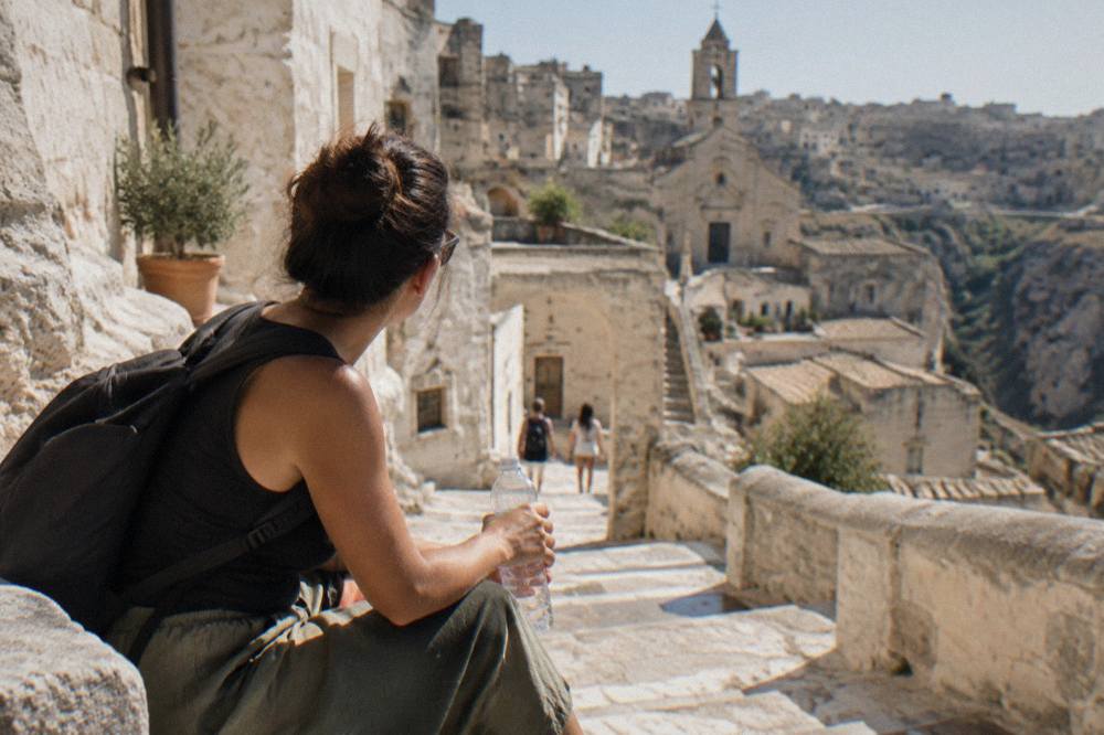A visitor holding a clear water bottle while resting on stone steps between whitewashed cave houses in Matera.