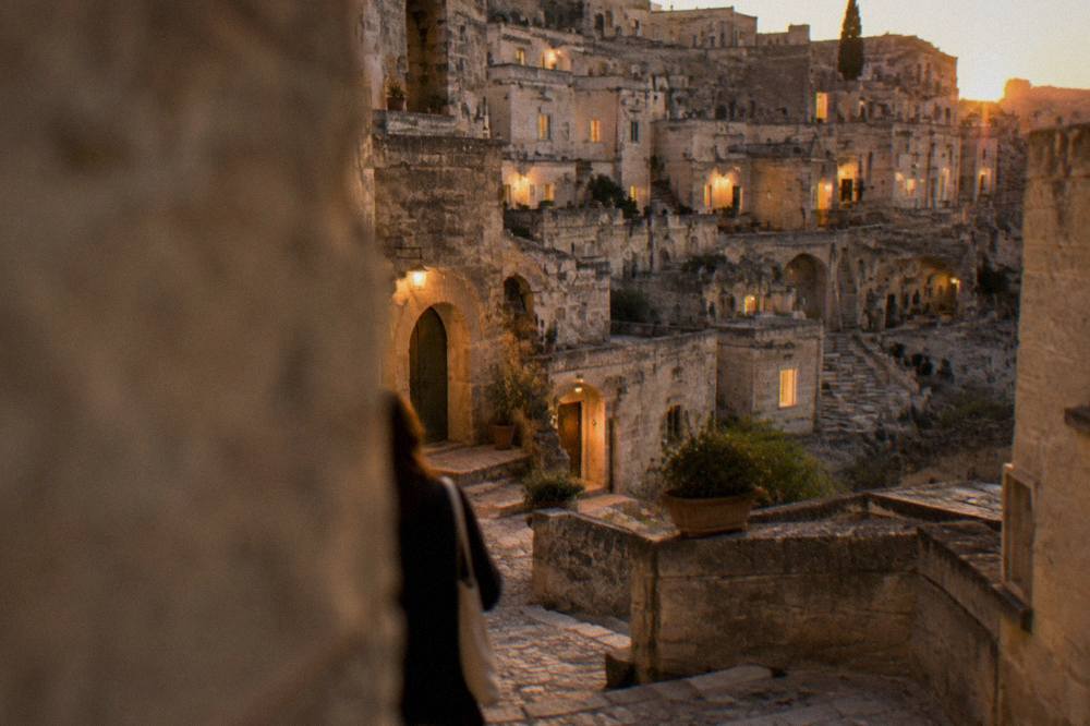 Lit windows of restored cave houses in Sasso Barisano seen from a street at dusk