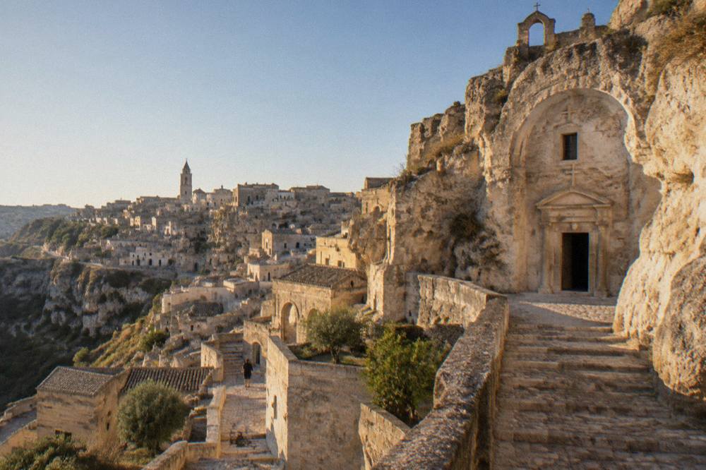 A rock-cut church facade and stone stairway in the Sassi district of Matera under a clear morning sky
