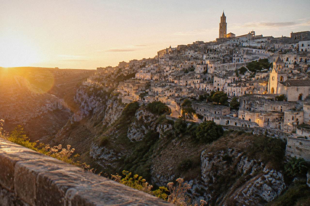 The Sassi district of Matera seen from across the Gravina canyon at dusk, with lit stone facades and rock-cut churches on the hillside
