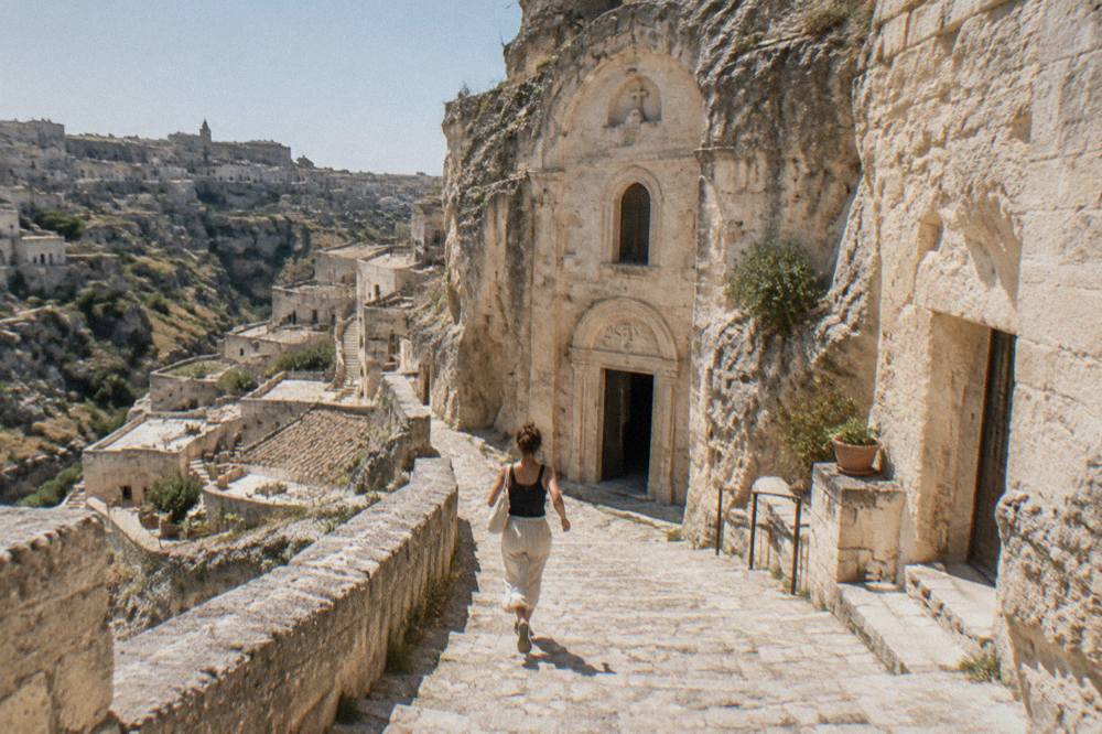A rock-hewn church facade carved into pale limestone above a stepped lane in the Sassi