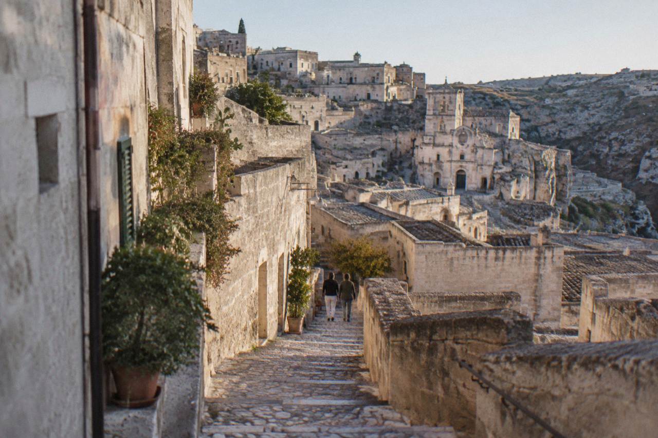 A stone staircase alley in the Sassi of Matera rising between pale tufa cave houses under a clear sky