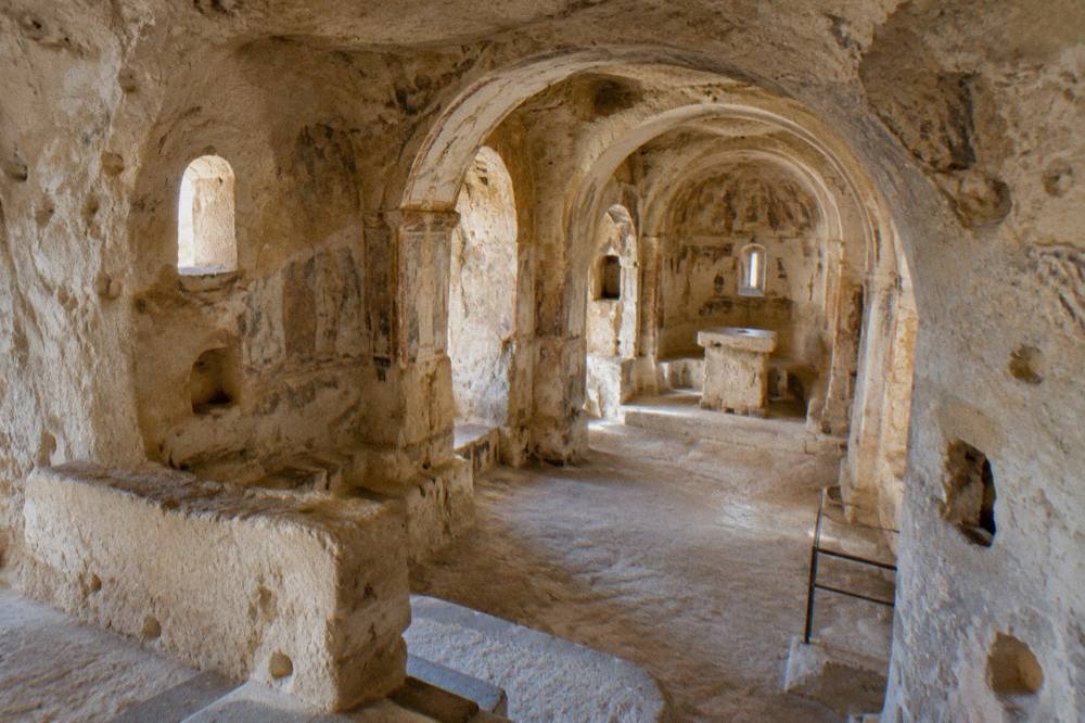 Interior of a rock-hewn rupestrian church in Matera with carved arches in pale limestone