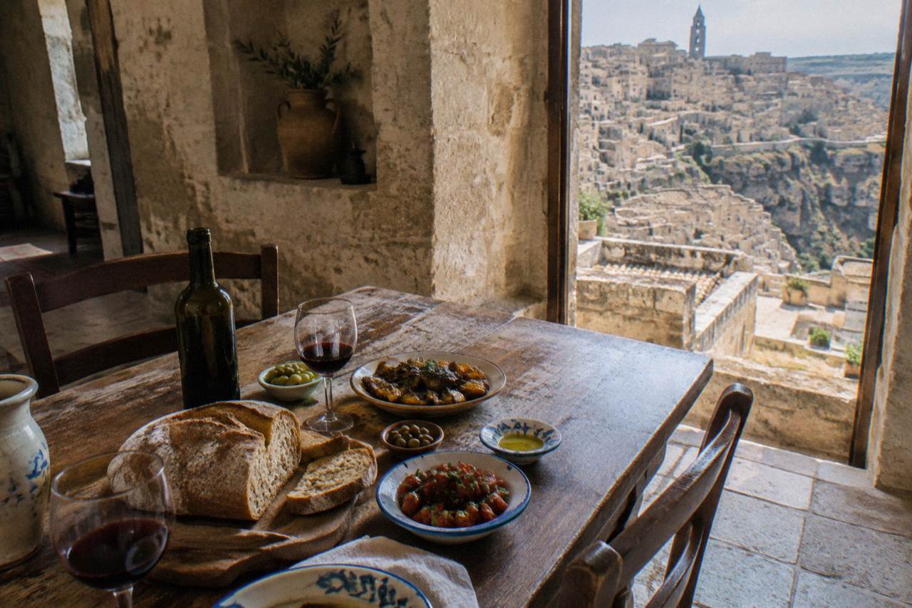 A rustic table set with bread, wine and simple dishes inside a stone dining room in Matera