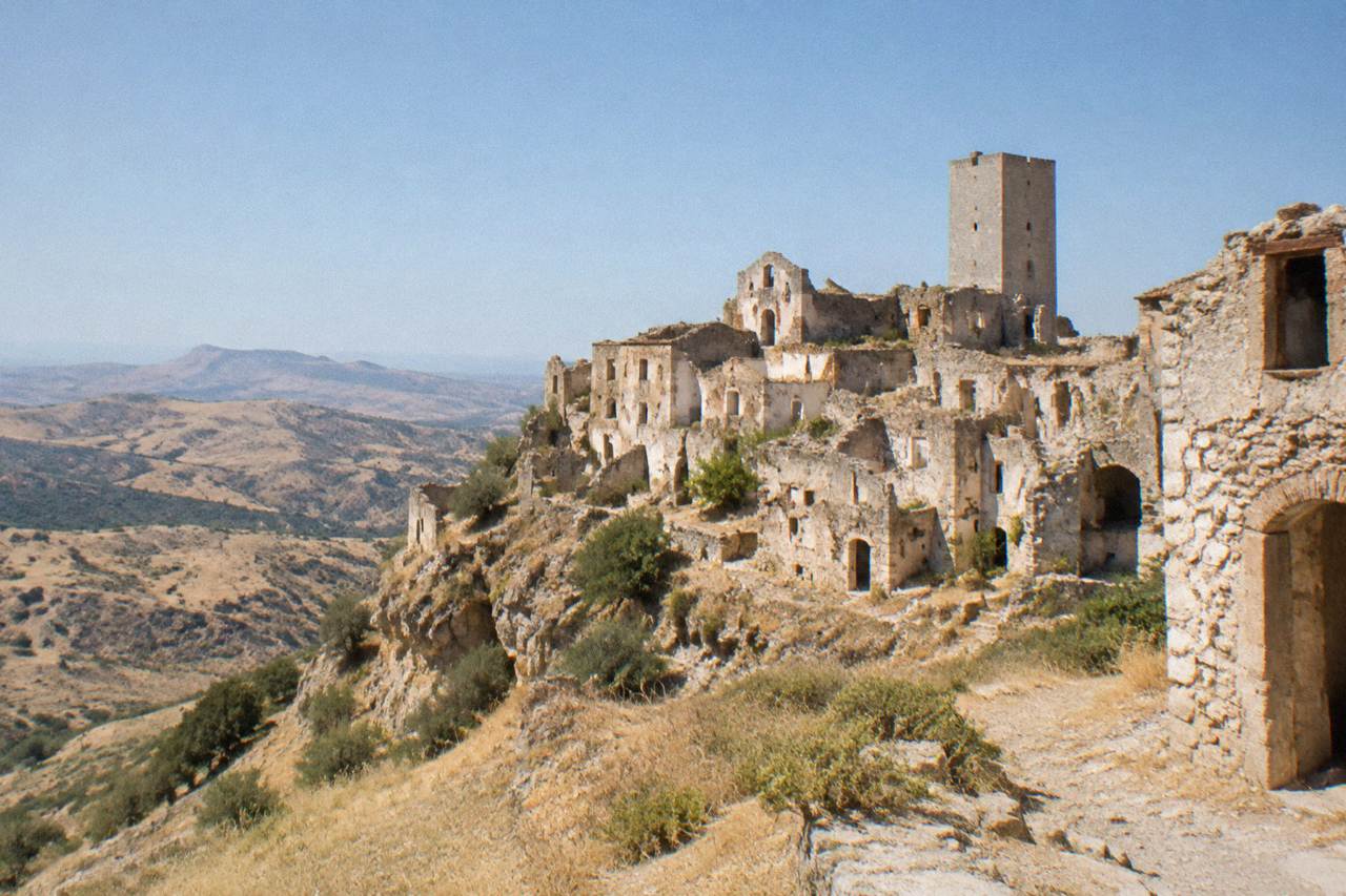 An abandoned stone hill town with empty houses and a tall bell tower rising above empty slopes