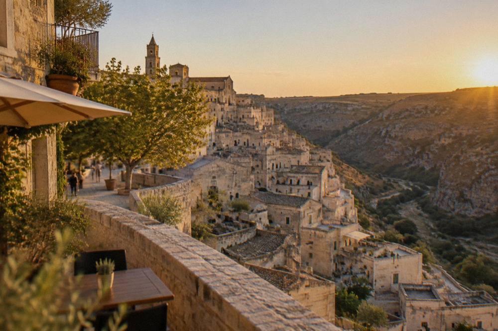 A view from a terrace over cave houses stacked down a hillside toward a canyon at golden hour