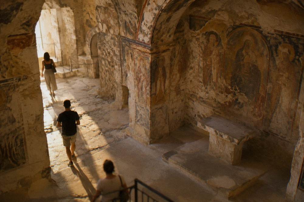 The interior of a rock-cut church with faded frescoes on stone walls