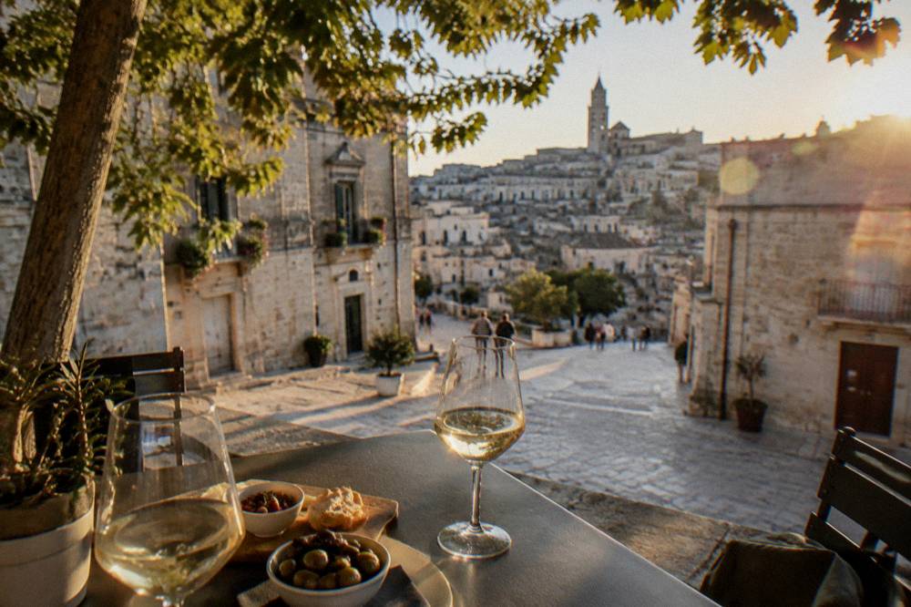 An outdoor table at dusk with wine glasses and small dishes overlooking stone buildings