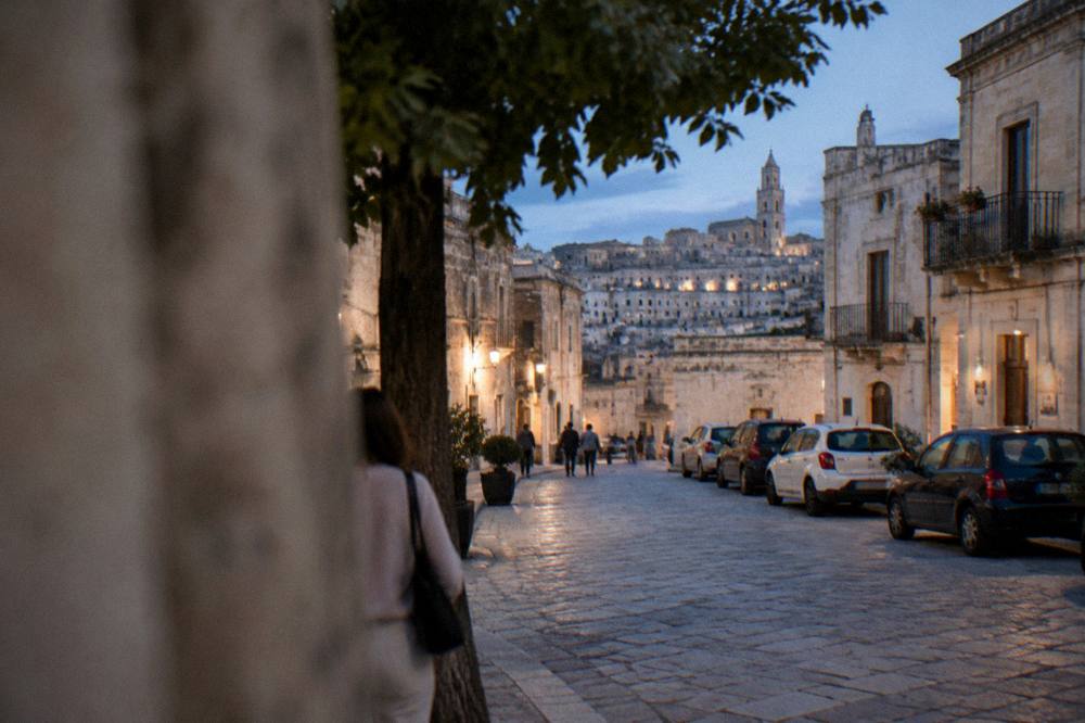 A stone street in southern Italy with parked cars along the edge and old buildings on both sides