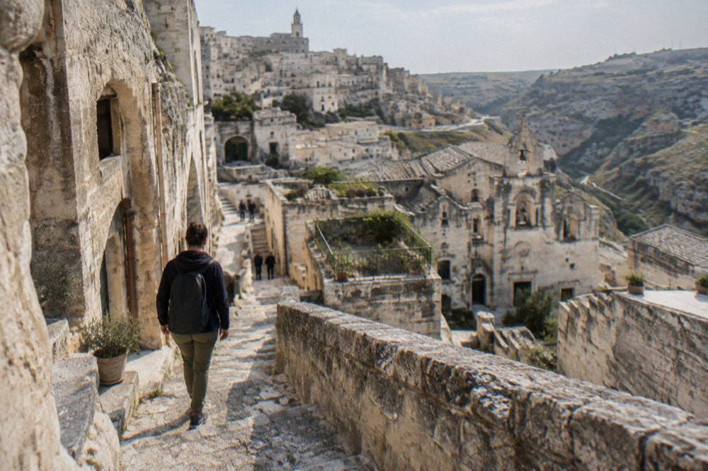 Visitor in sturdy shoes stepping down a worn stone staircase between cave facades in Matera