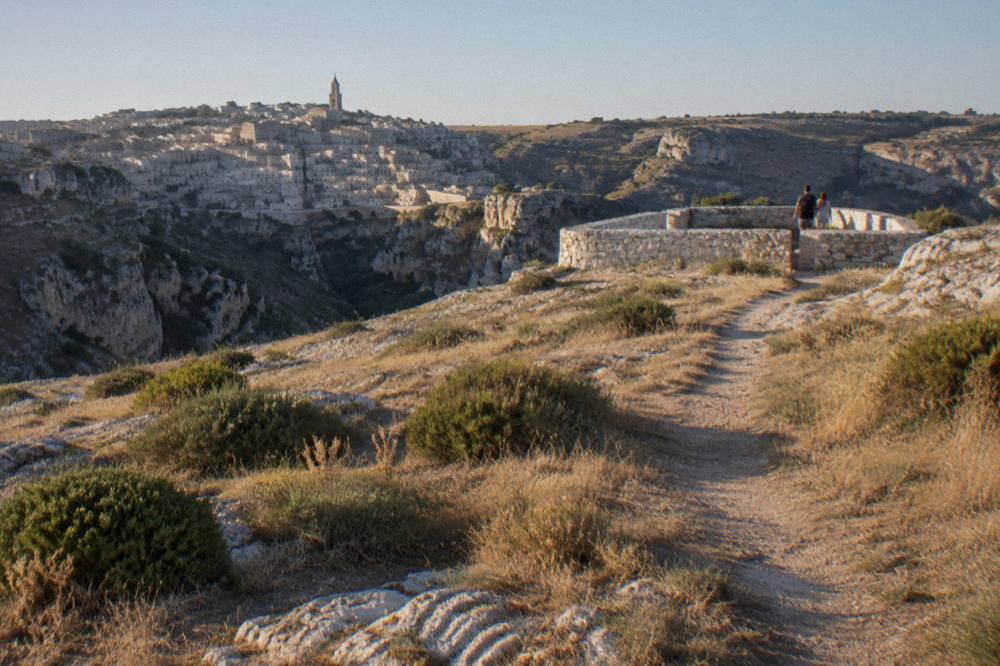 A narrow dirt path across dry grassland toward a stone enclosure on a plateau