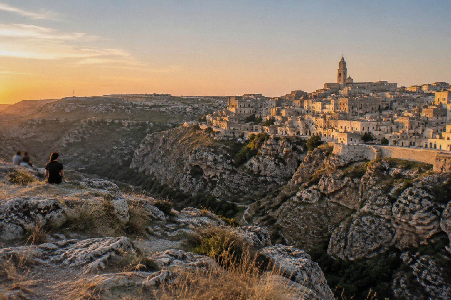 View across the Gravina canyon from the Murgia plateau toward the lit Sassi at dusk