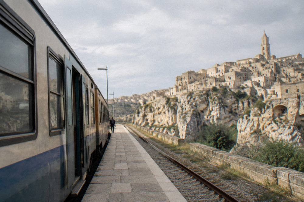 A single-track regional train standing at a small station platform in southern Italy
