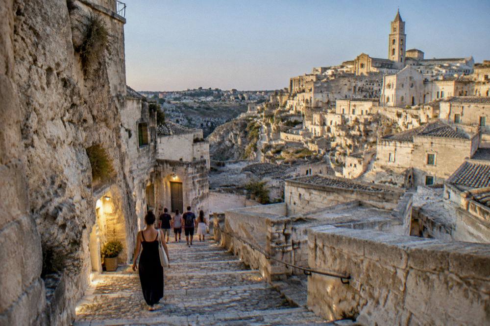 Visitors walking down a stone stairway between cave houses in Matera