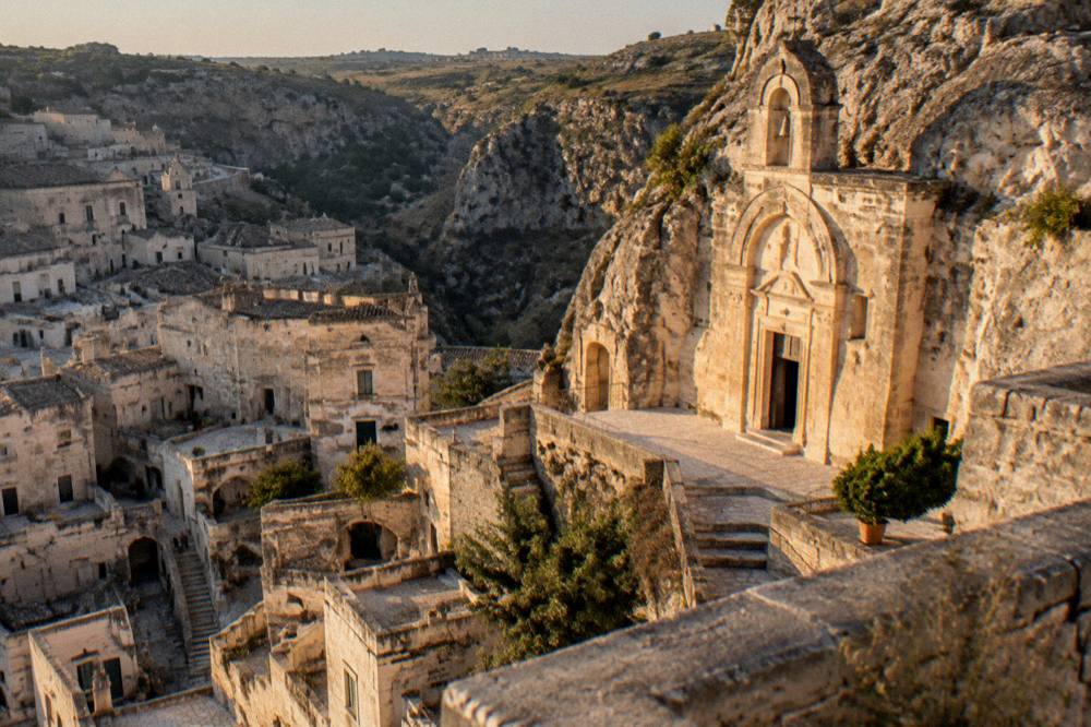 The facade of a rock-cut church lit by evening light above the Sassi of Matera