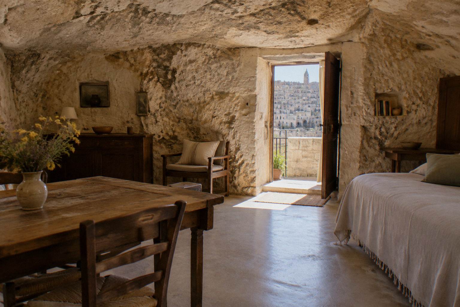 Interior of a furnished cave house with a rough rock ceiling and simple wooden furniture