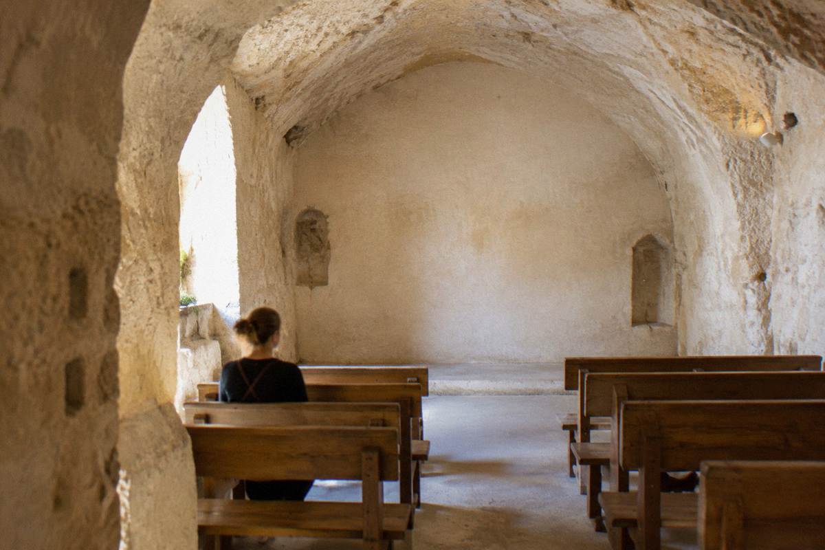 Small vaulted cave room fitted with benches facing a plain wall, soft light