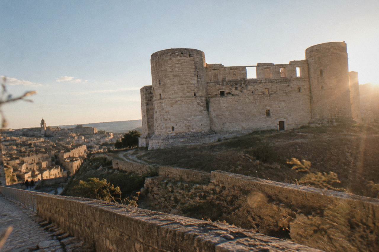 The unfinished facade and round towers of Castello Tramontano on the edge of Matera under an open sky