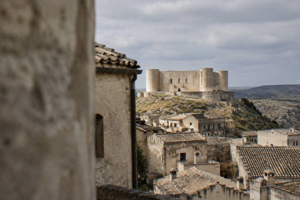 The castle seen from a Matera street with tiled roofs and the Murgia plateau on the horizon
