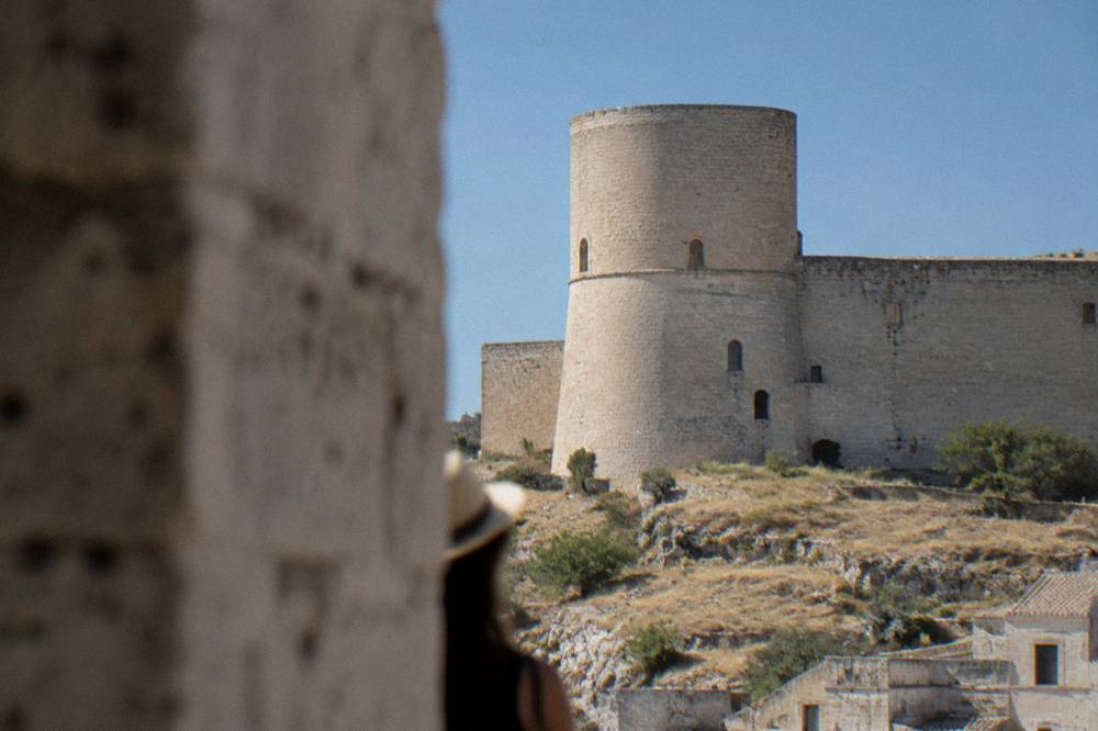 A round tower of the castle against a clear blue sky seen from the surrounding hill