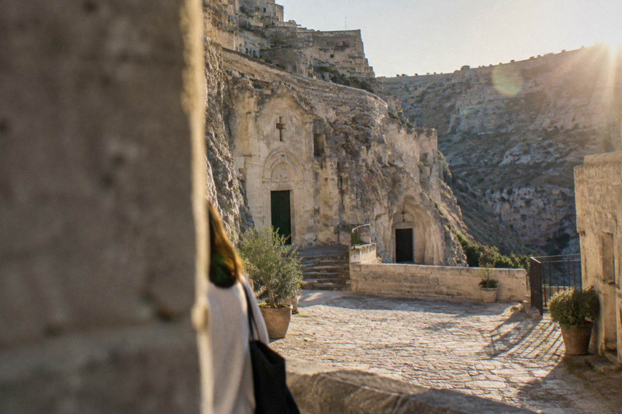 A sunlit stone courtyard in the Sasso Caveoso of Matera with rock-hewn church facades carved into pale tufa