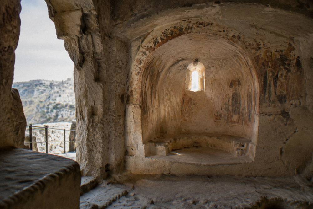 A hollowed cave church interior with a carved stone apse and soft light entering from a small opening
