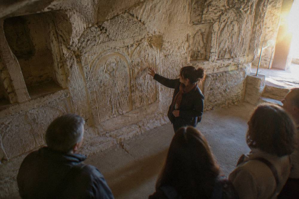 Guide explaining carvings to a small group in an underground chamber