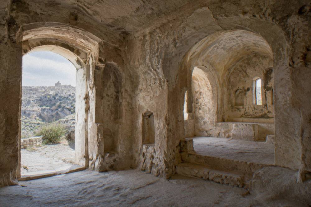 A rock-cut church interior with pale stone walls and arched niches lit by natural light