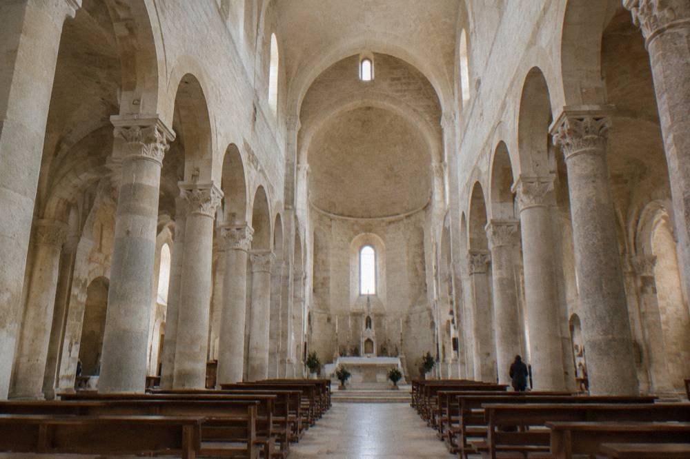 The interior of Matera Cathedral with stone columns, arches and an altar lit by daylight