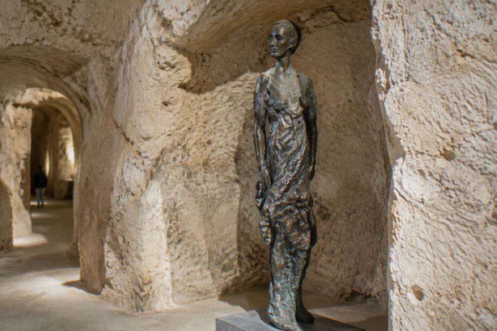 Bronze sculpture standing in a rock-cut alcove with rough stone walls