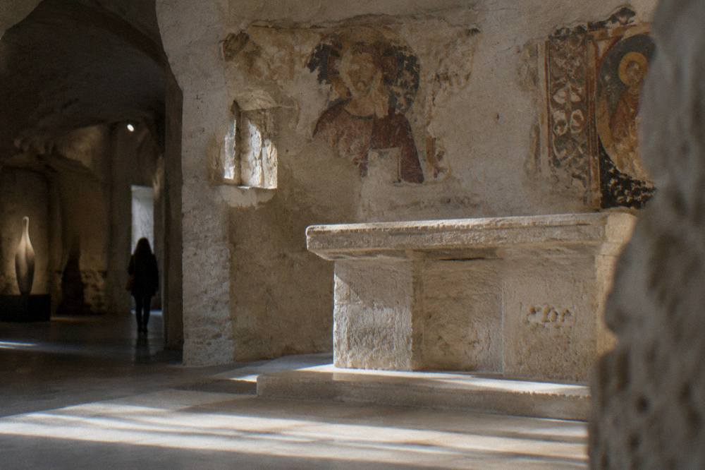 Interior of a rock-cut church with fresco fragments above a stone altar