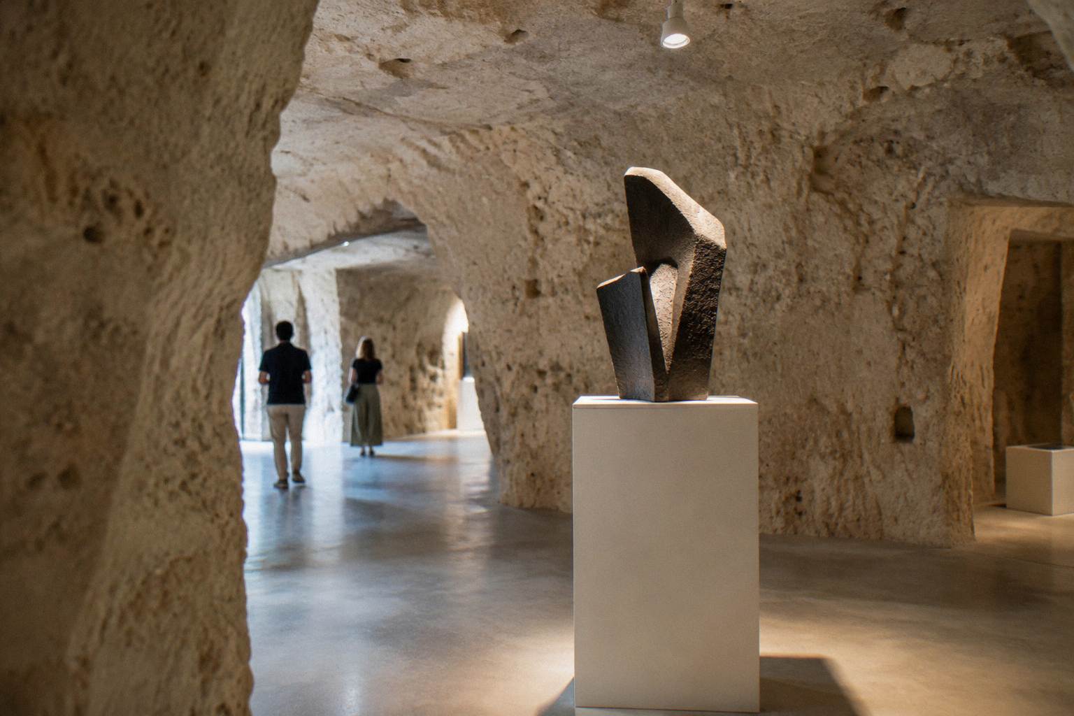 Gallery room cut into rock with a modern sculpture on a plinth, lit from above