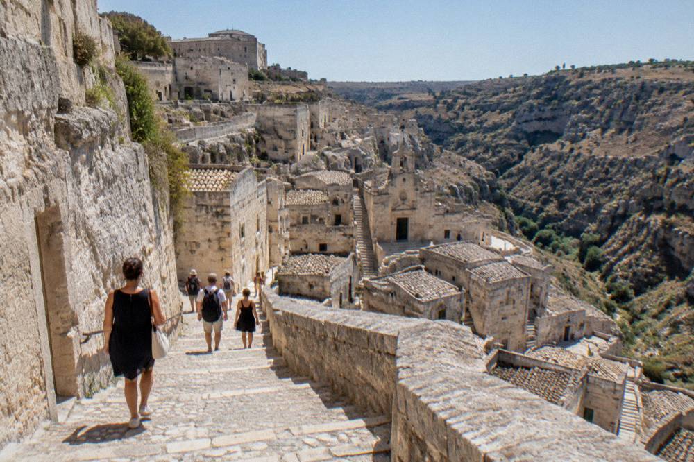 Visitors walking down a stepped stone lane from the palace rim into the Sasso Caveoso