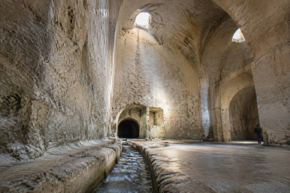Rainwater canal carved into pale limestone rock leading toward a cistern mouth