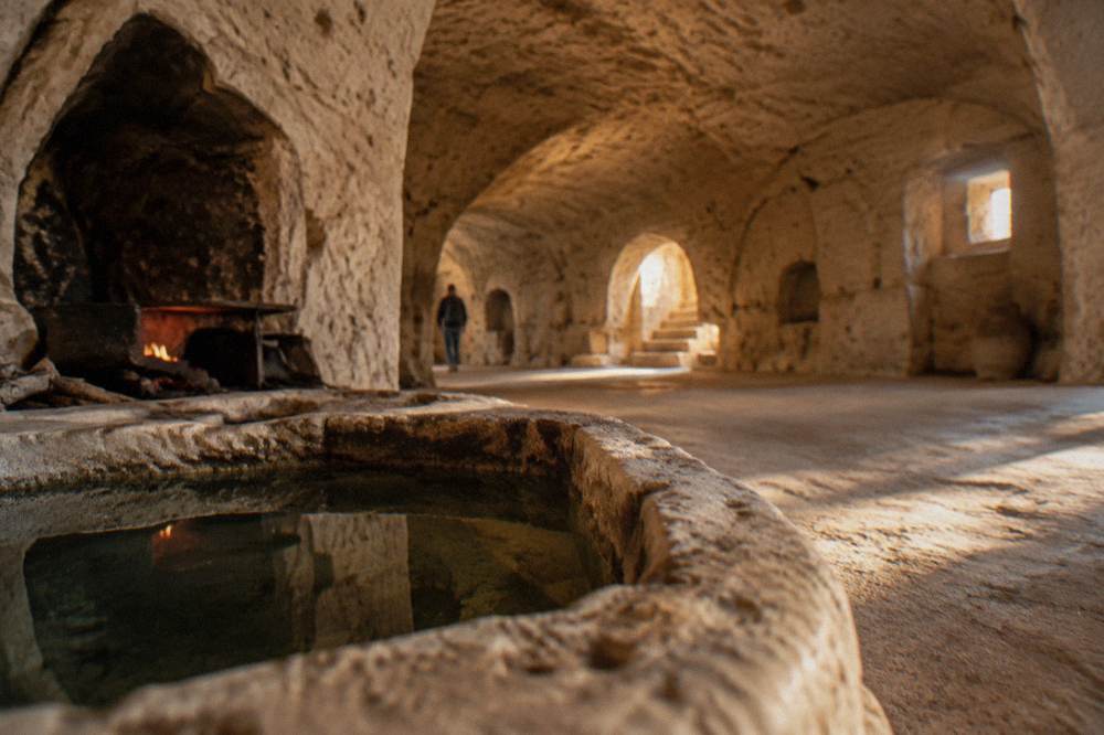 Interior of a cave dwelling with a small stone water cistern beside a hearth