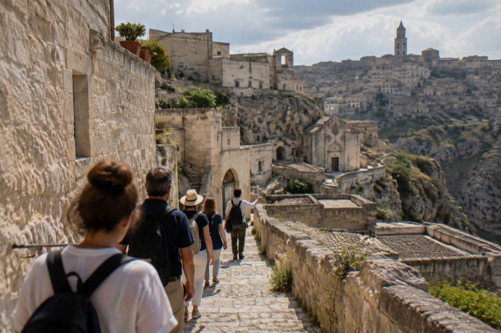 Tour group with a guide walking a narrow stepped lane between pale stone houses in the Sassi
