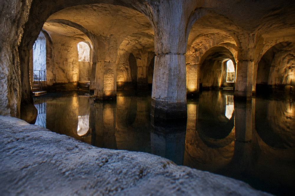 Wide view of a pillared underground water cistern lit warmly, arches reflected in dark still water