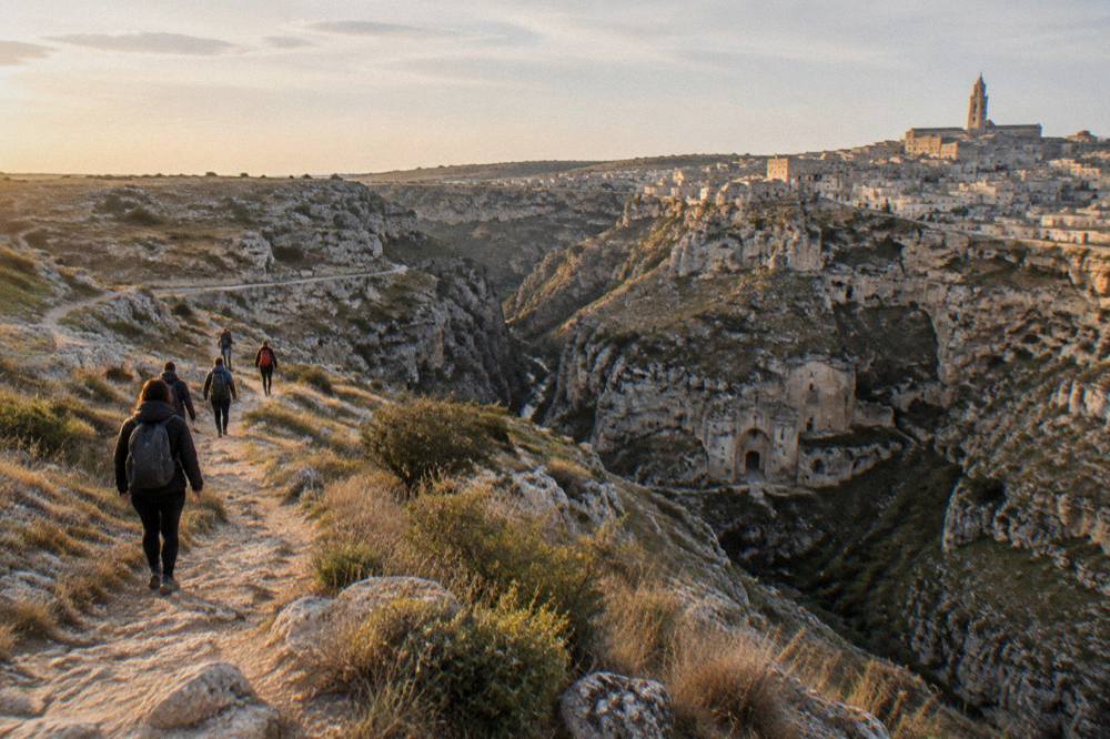 Hikers on a stony path above a deep canyon at golden hour
