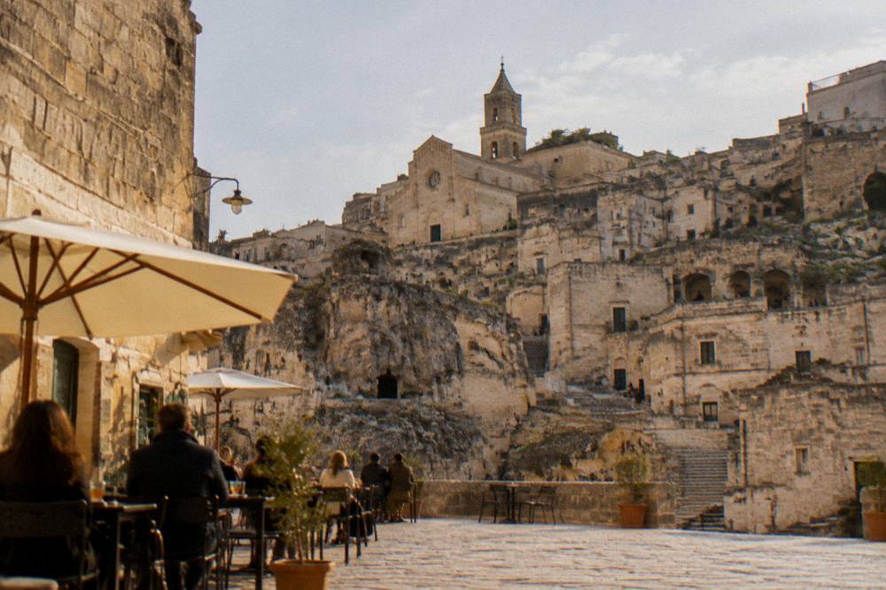 Cafe tables and people on a stone square in Matera in the early evening with warm light