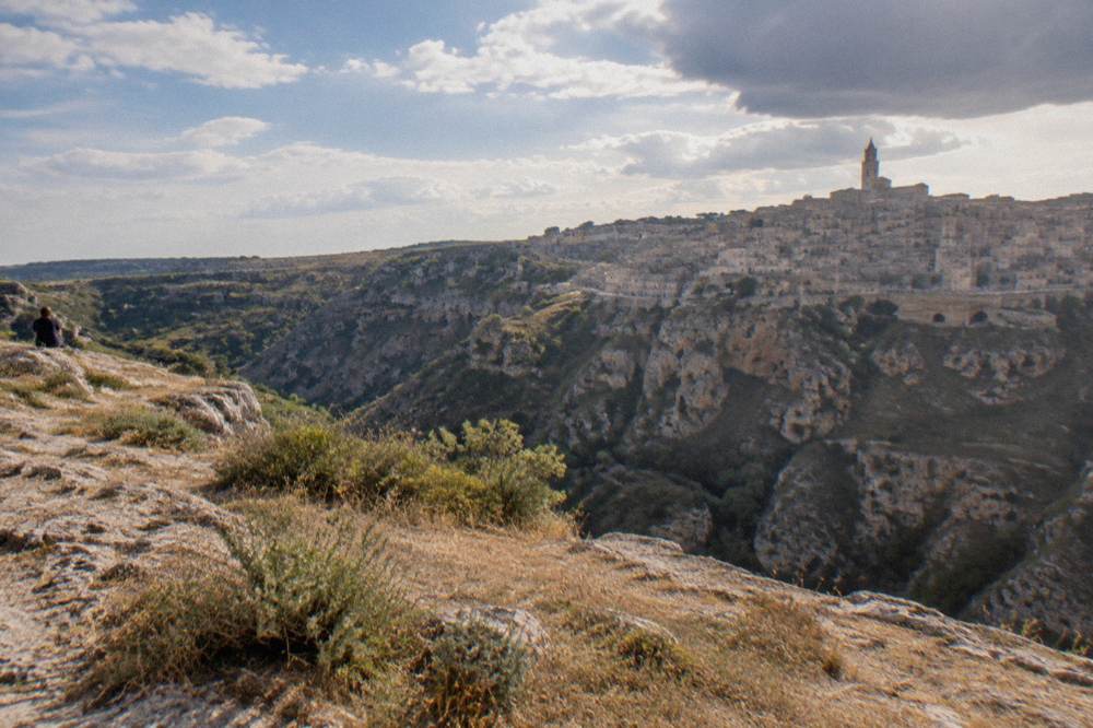 Dark openings of cave chapels in the limestone cliff across the Gravina gorge