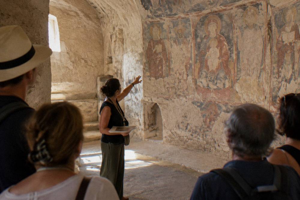 Licensed guide explaining a fresco to a small group inside a Matera cave church