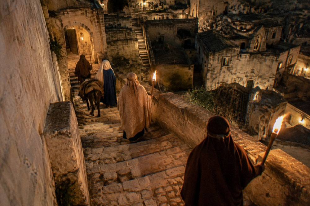 Costumed living nativity figures on a torchlit stone stairway in the Sassi of Matera at night