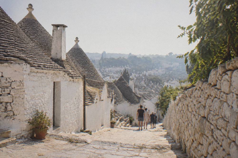 Cone-roofed trulli houses of Alberobello seen across a dry-stone-walled lane in the Itria Valley