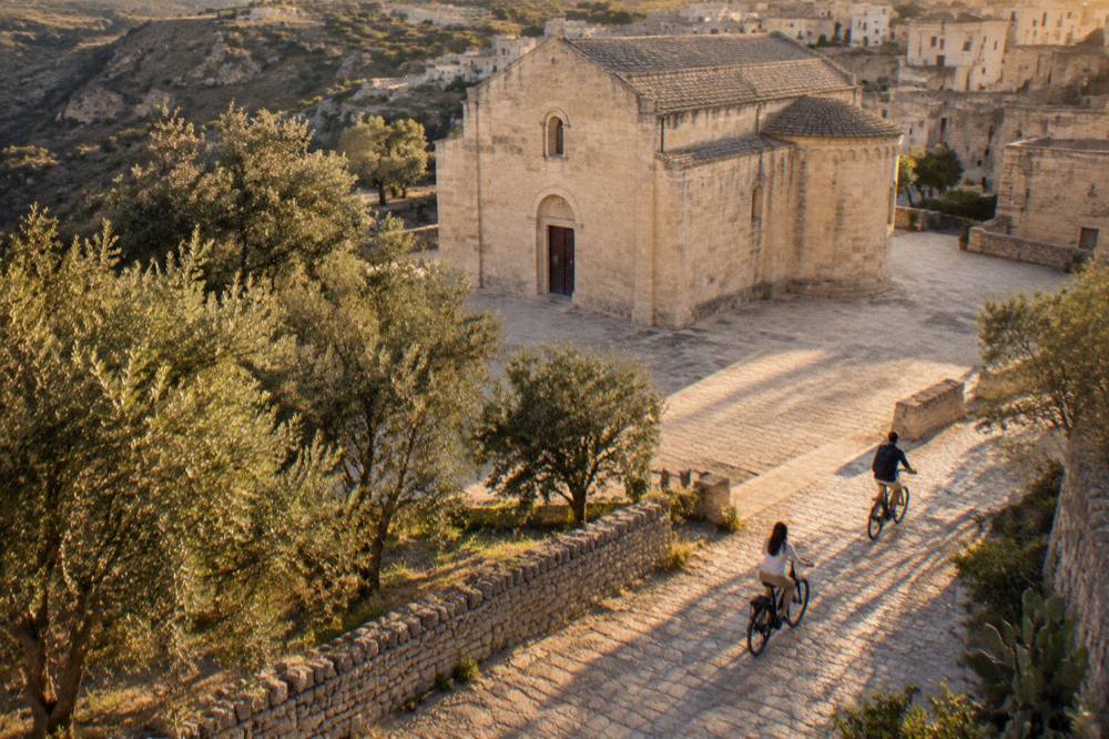 Riders on electric bicycles rolling past olive trees and stone walls in the countryside of southern Italy